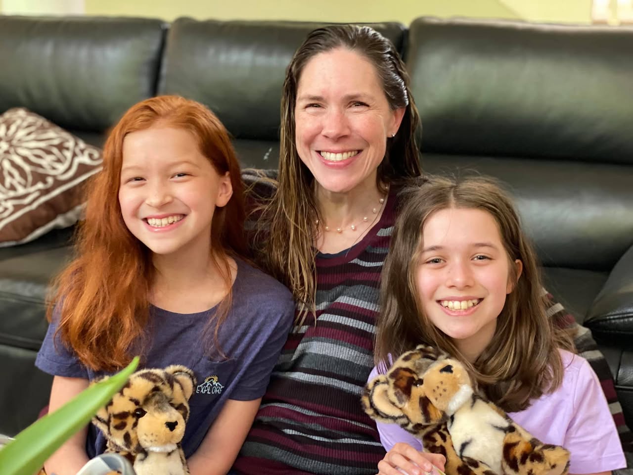 A family of three smiles on a black leather couch, each holding a stuffed tiger toy.