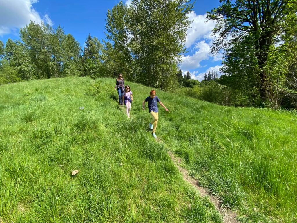 A family enjoying a walk up a grassy hill in the Pacific Northwest.