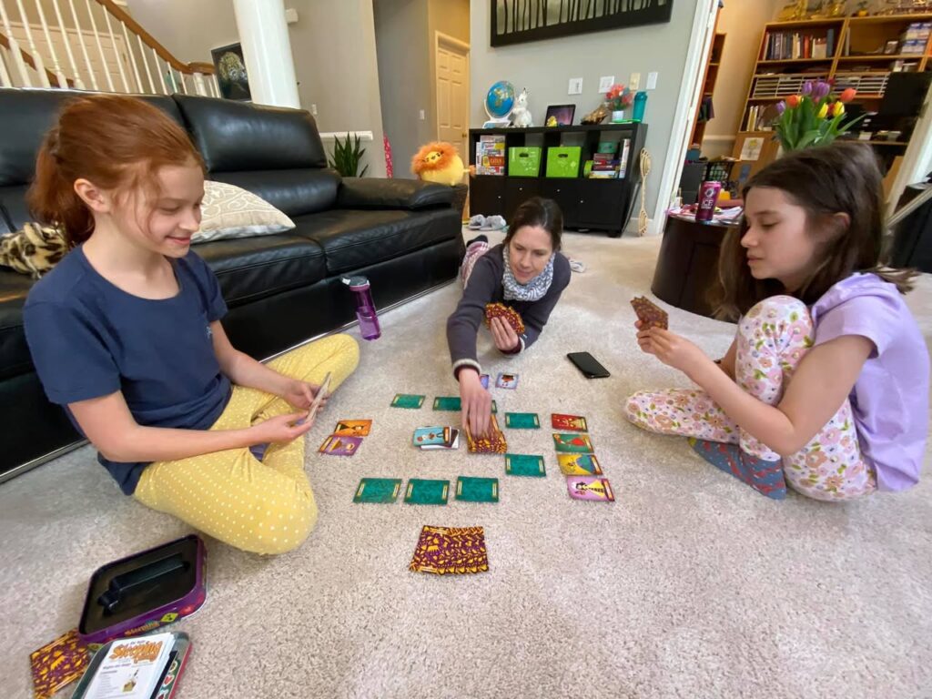 Three people playing a card game on the floor in a cozy home setting.