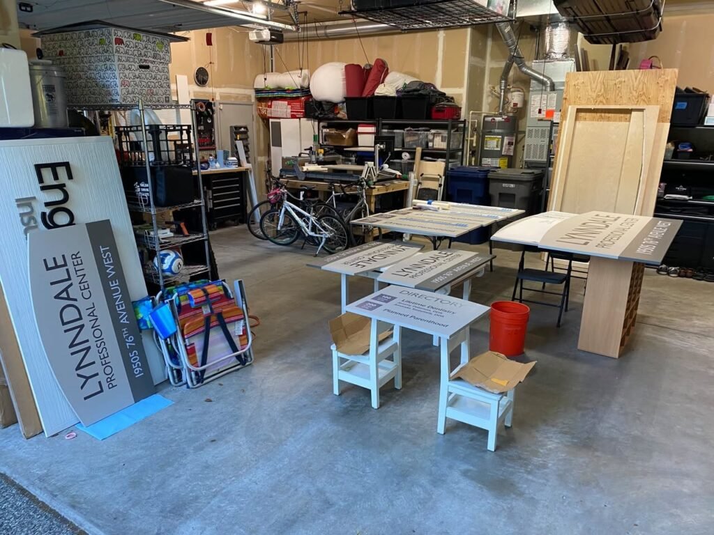 Children's table and chairs on display in a woodworking workshop. Project signage visible in the background.