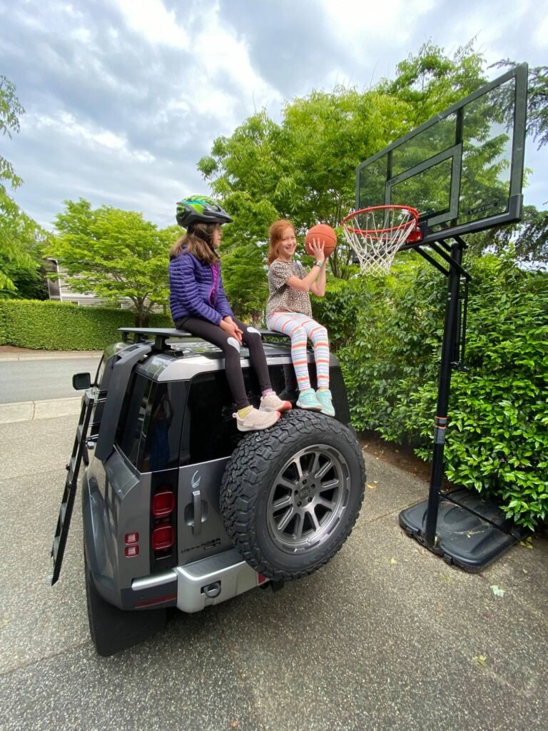 Two kids play basketball on a driveway basketball hoop.