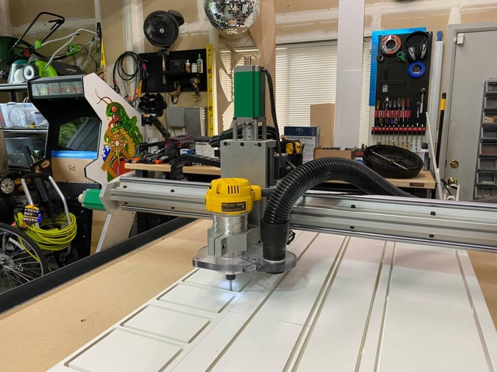 A CNC router cutting a design into a white panel in a well-eqipped garage workshop.