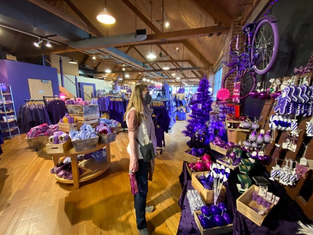 A shopper browses purple merchandise inside a wooden retail space with rustic beams and hanging lights.
