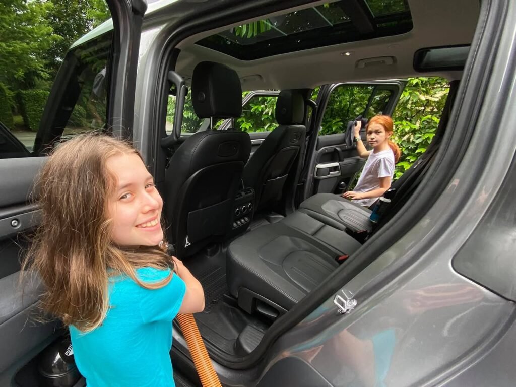 A smile is captured beside an open Jeep door with green foliage in the background. The image highlights a candid travel moment near the Pacific Northwest.