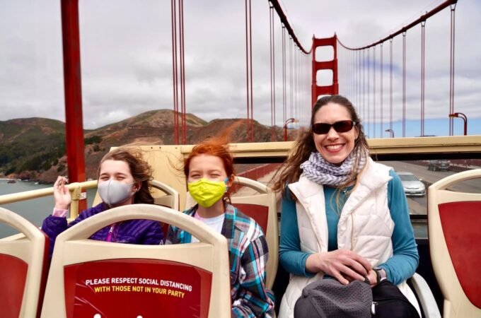 A family wearing masks on a ferry with the Golden Gate Bridge in the background. A scenic view of the iconic suspension bridge in San Francisco.