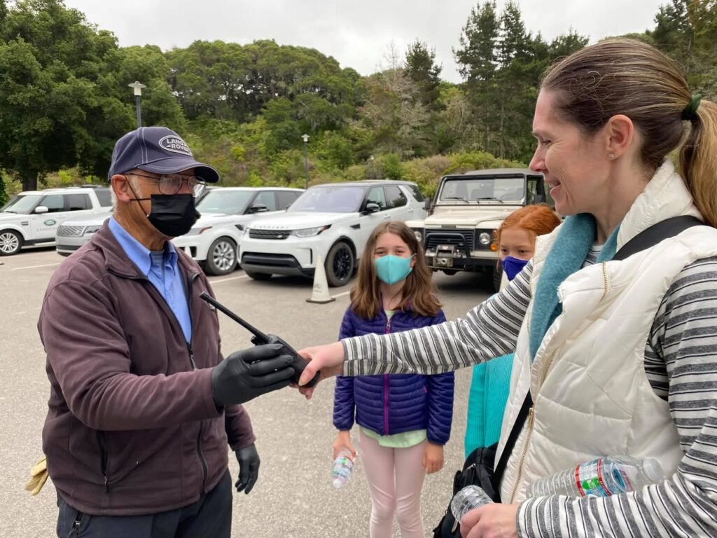 A person receiving a vaccine in an outdoor parking lot surrounded by cars and trees.