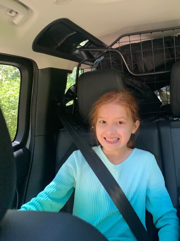 A happy child wearing a seatbelt in the back seat of a vehicle during a family road trip.