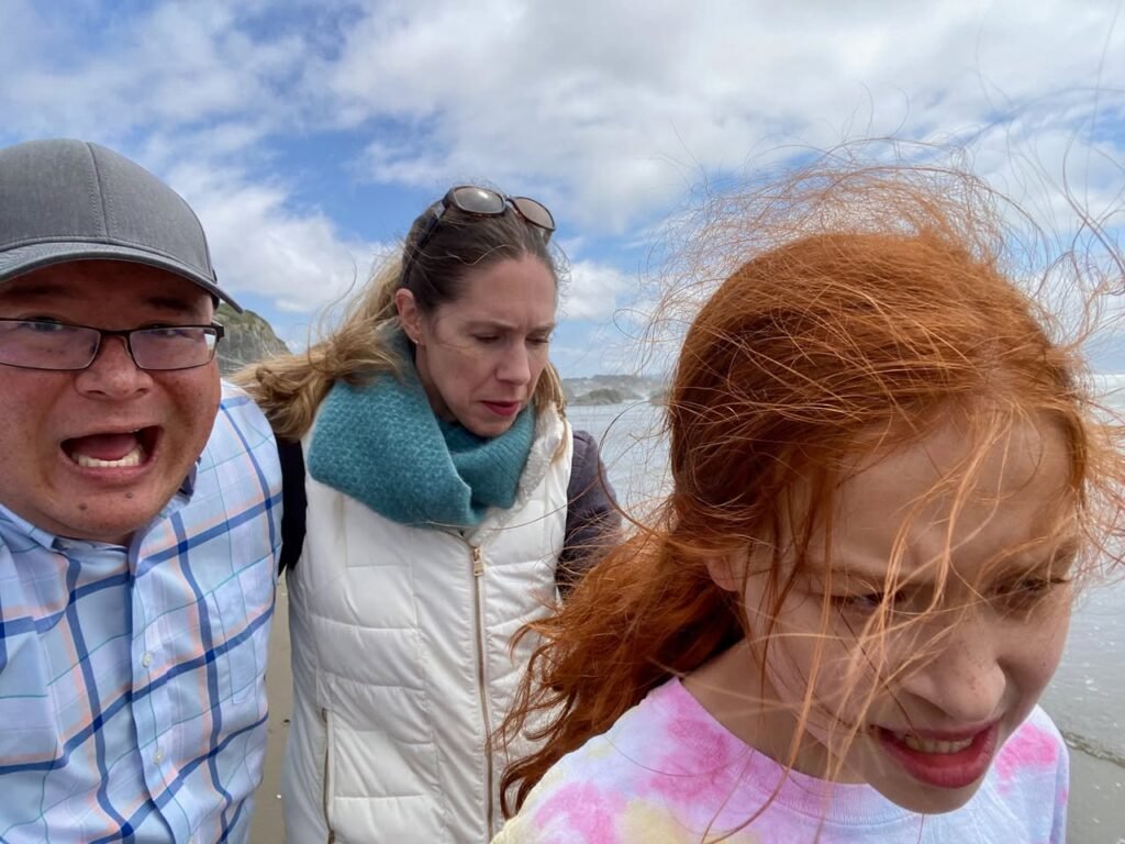 A family enjoys a breezy coastal adventure with hair blowing in the wind against a backdrop of blue sky and ocean waves.