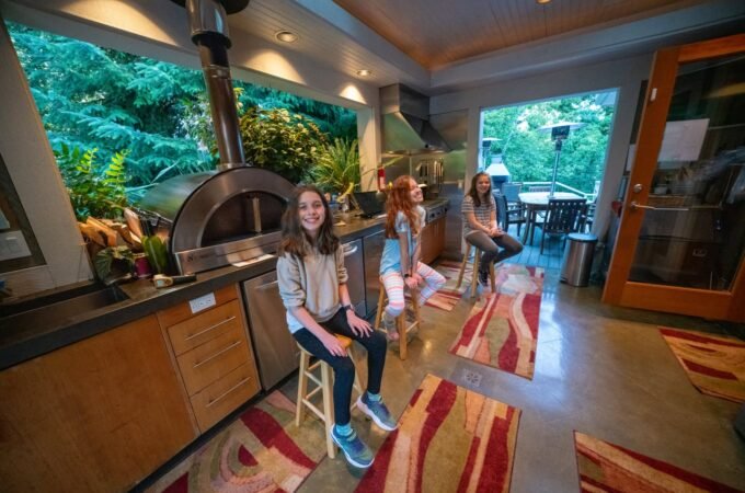 A cozy indoor dining space at Barefoot Ranch in Portland with large windows opening to lush greenery. People sit on stools and look out at the nature view.