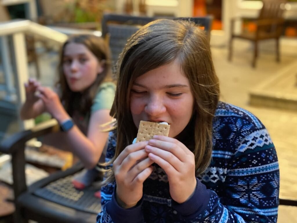 A person in a patterned sweater enjoying a cracker on a sunny outdoor deck.