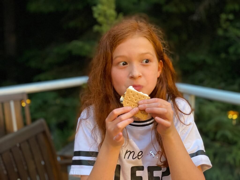 A person enjoying a grilled cheese sandwich on a wooden deck surrounded by green foliage.