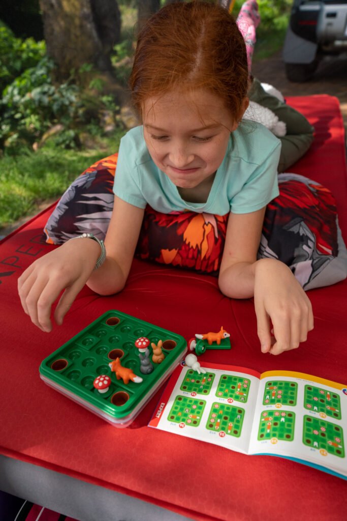 A young red-haired person plays a tabletop garden game on an outdoor table.