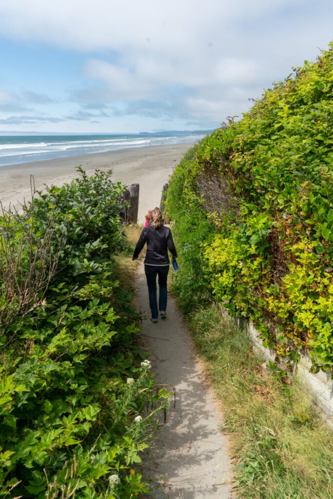 A coastal boardwalk with lush greenery leading to the ocean under a cloudy sky.