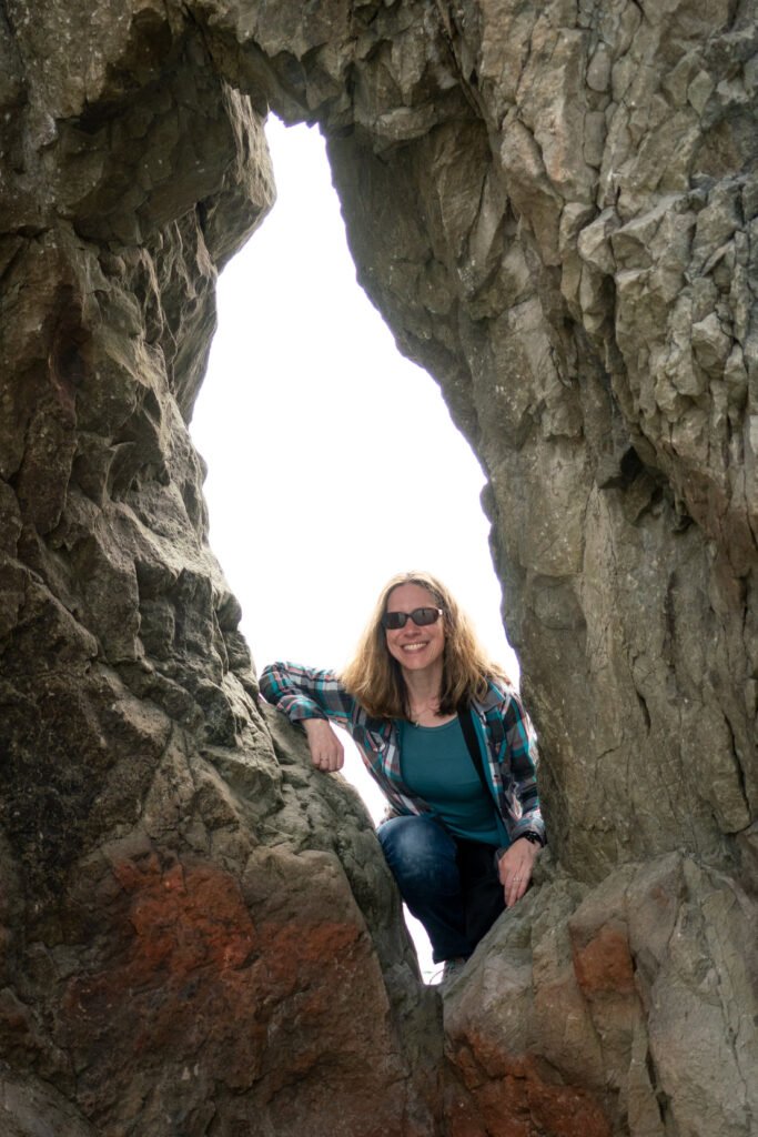 A person poses within a rugged natural rock arch formation, framed by textured stone.