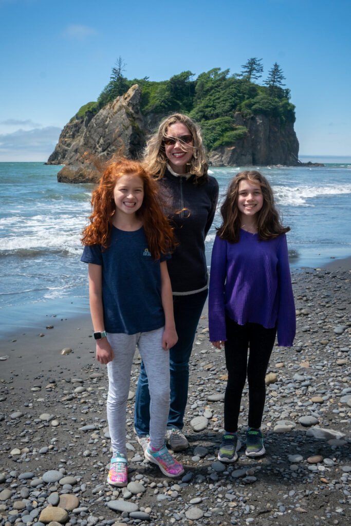A family encoys a sunny-day visit to a rocky coastline, posing in front of lush sea stacks.