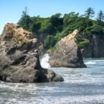 A foggy view of a Pacific Northwest rocky island surrounded by turquoise waves. Giant rock formations are partially visible in the mist.