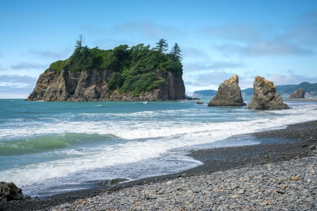 A pebbled beach with gentle waves breaking near a lush, rocky island in the distance.