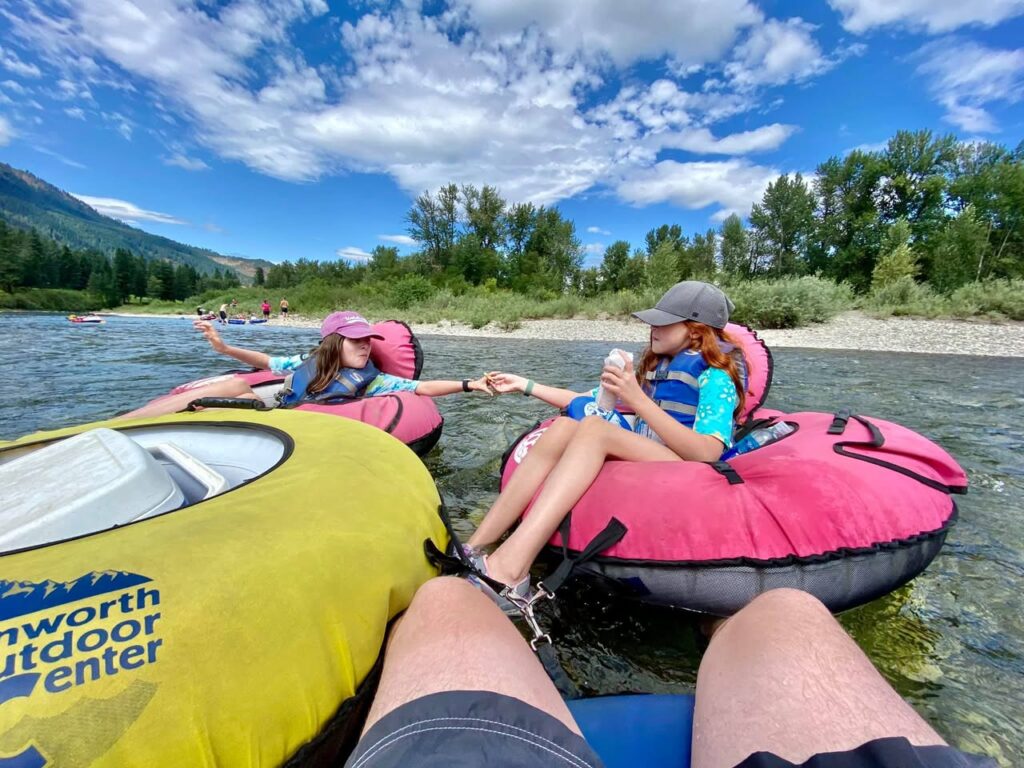 People relaxing in colorful inner tubes on a scenic river with mountains in the background.