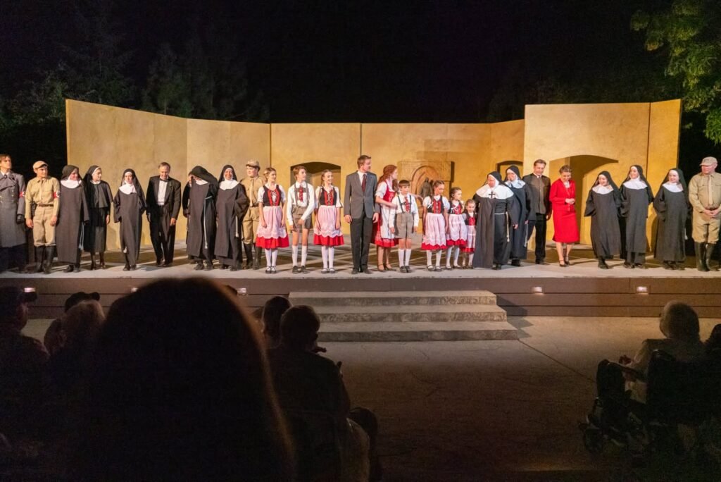 Actors in vintage and religious costumes perform under the night sky at an outdoor amphitheater.