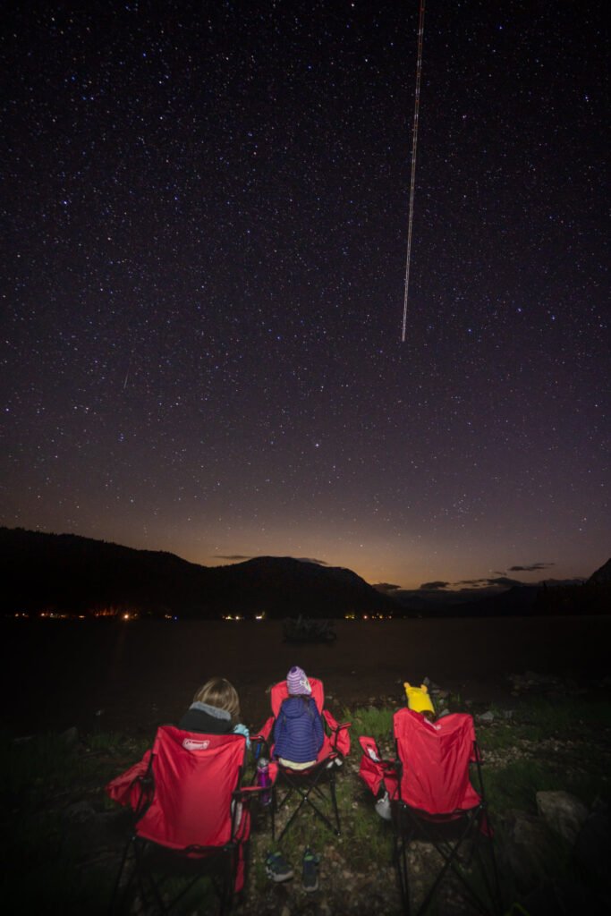 People in red chairs watching the night sky with stars and a bright meteor.