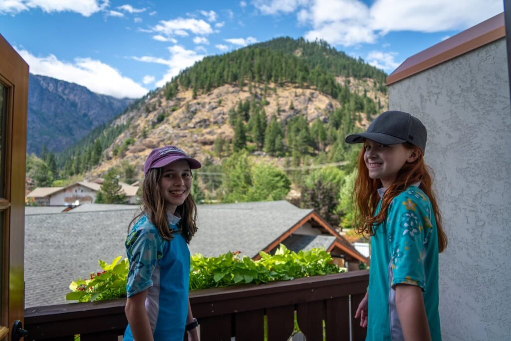 Two people enjoying a mountain view from a balcony. Scenic backdrop of forested slopes and a small cabin.