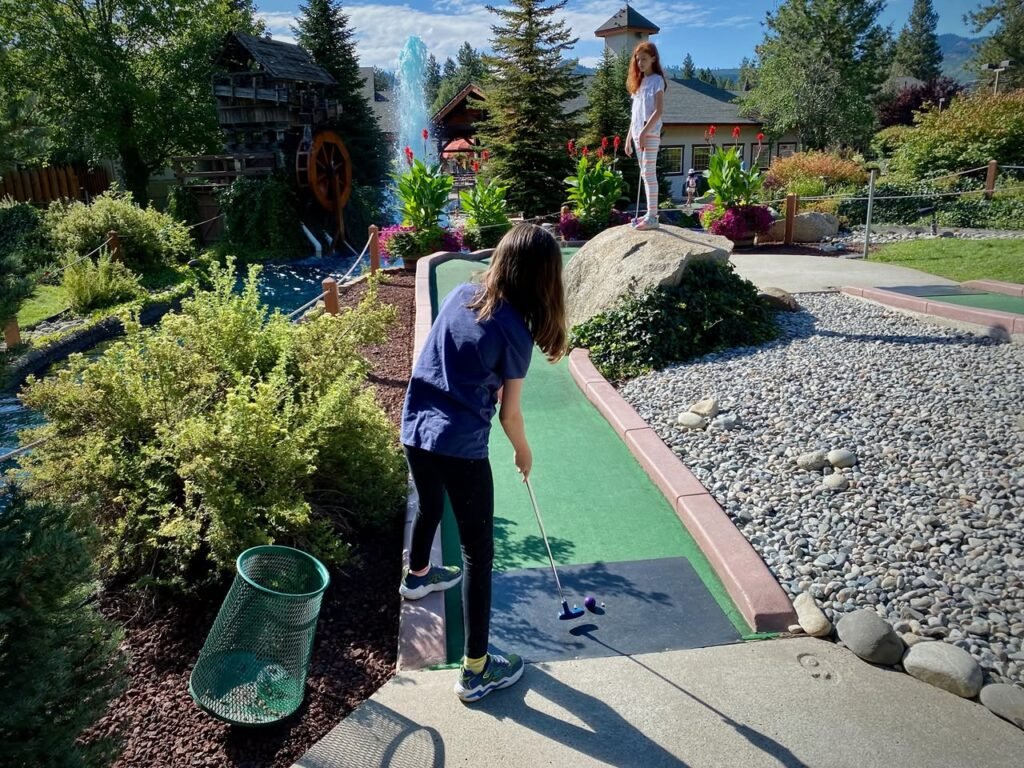 Kids playing miniature golf near a large mountain stream.
