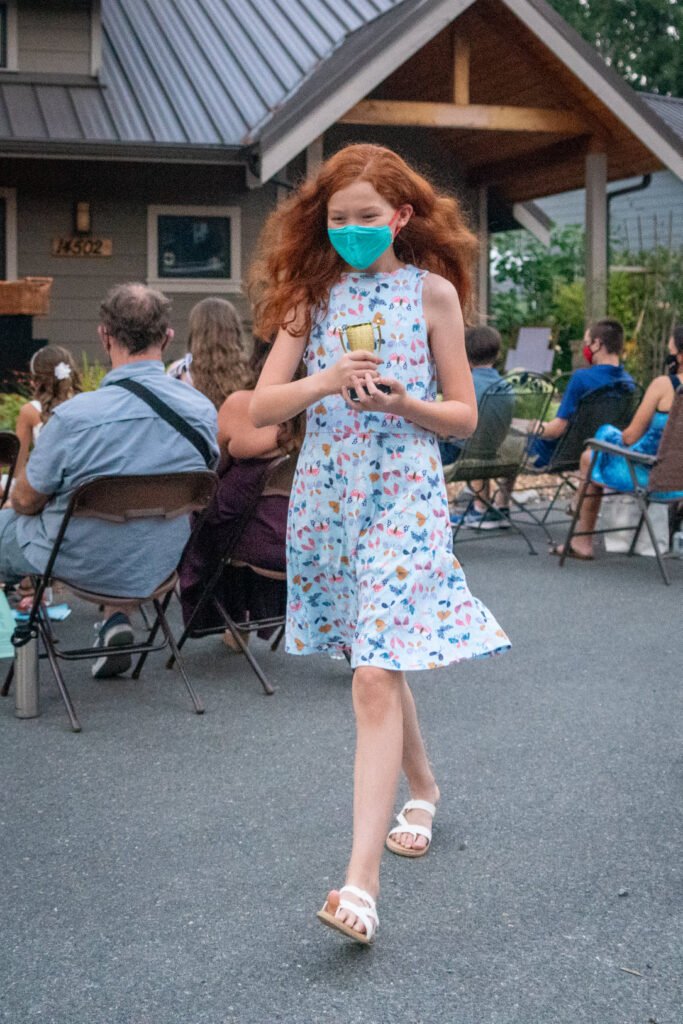 A person in a floral dress wearing a teal face mask walks through a courtyard during an outdoor event.