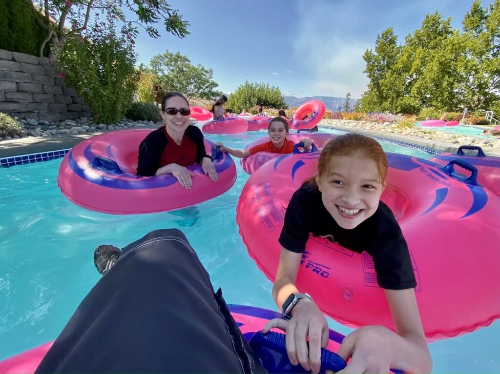 People relaxing on pink flamingo tubes in a lazy river at a water park on a sunny day.