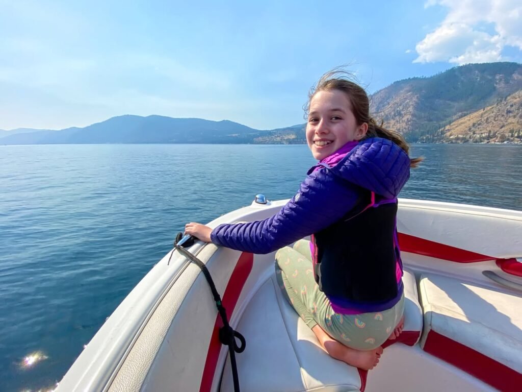 A person enjoys a sunny boat ride on calm waters with mountains visible in the distance. The scene captures the beauty of the Pacific Northwest.