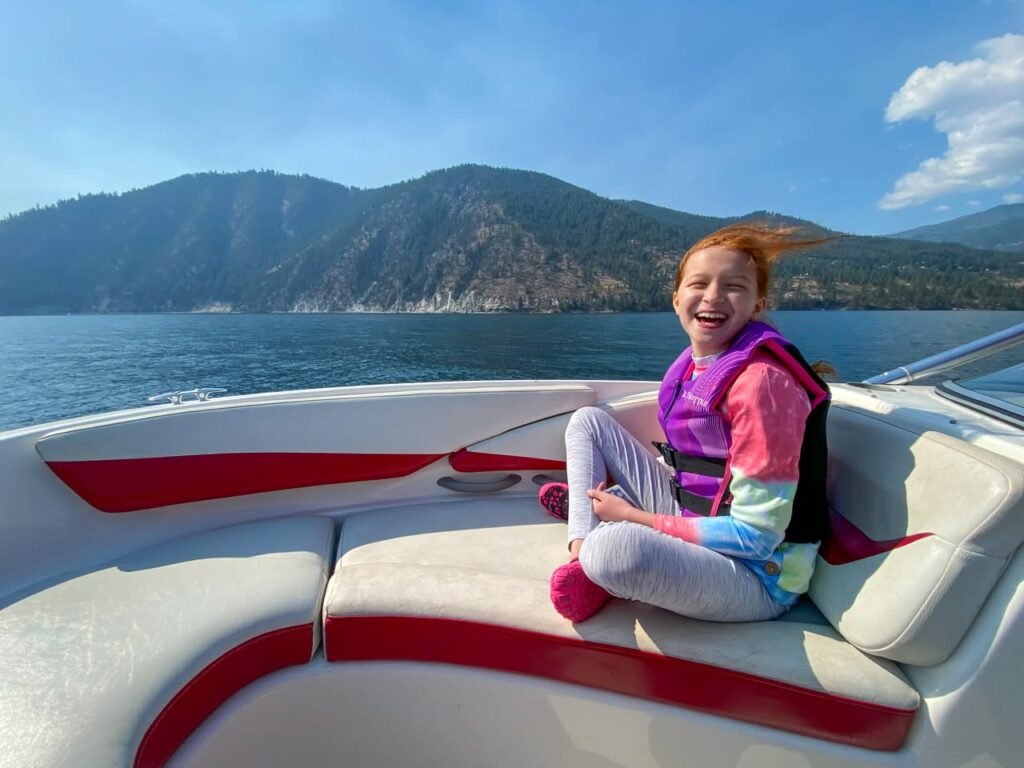 A person wearing a life vest enjoys a boat ride on the water with mountainous coastline scenery in the background.