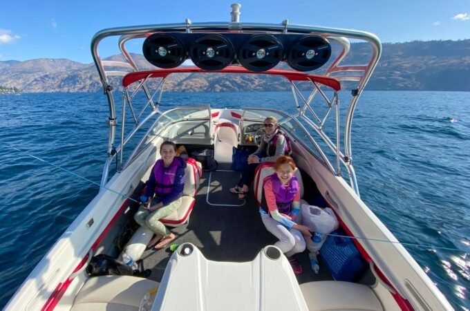 A group enjoying a day on a white speedboat with red accents, cruising on calm blue water with mountains in the distance.