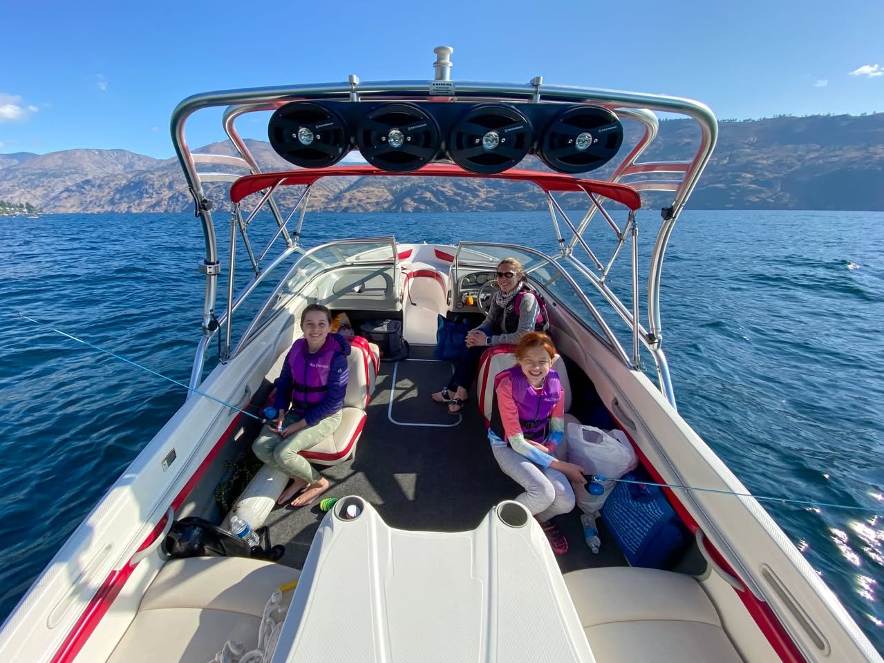 Boating Lake Chelan A group enjoying a day on a white speedboat with red accents, cruising on calm blue water with mountains in the distance.