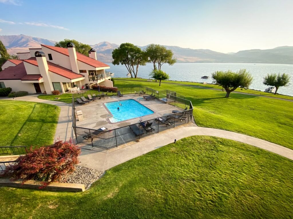 A modern home with a well-maintained lawn and an outdoor pool overlooking a lake and distant mountains.