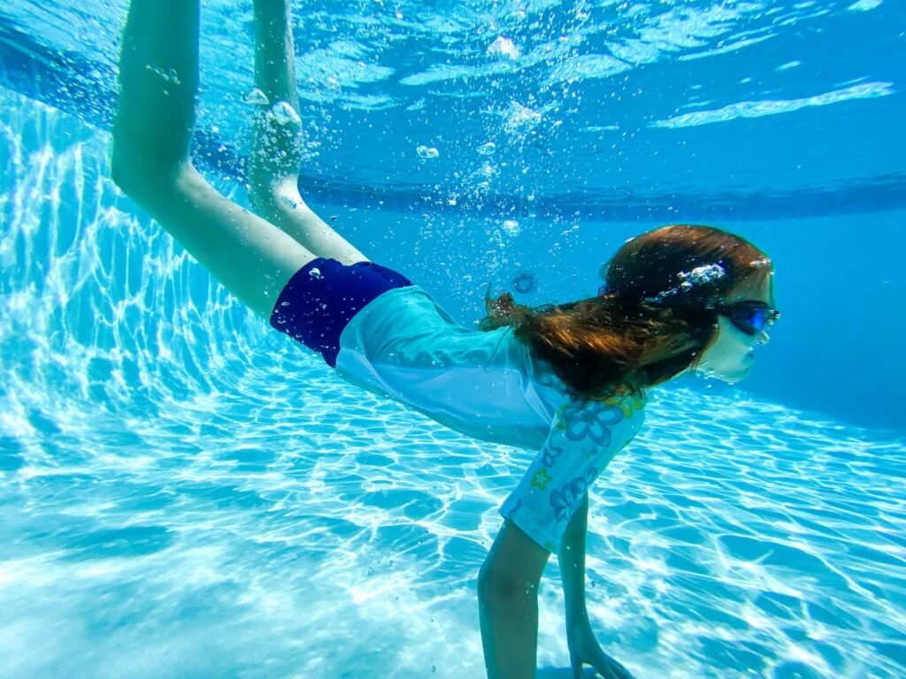 A person swimming underwater in a clear blue pool.
