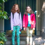 Lake Chelan Vacation Home Two girls standing on the porch steps in front of a dark blue door, wearing colorful outfits and backpacks.