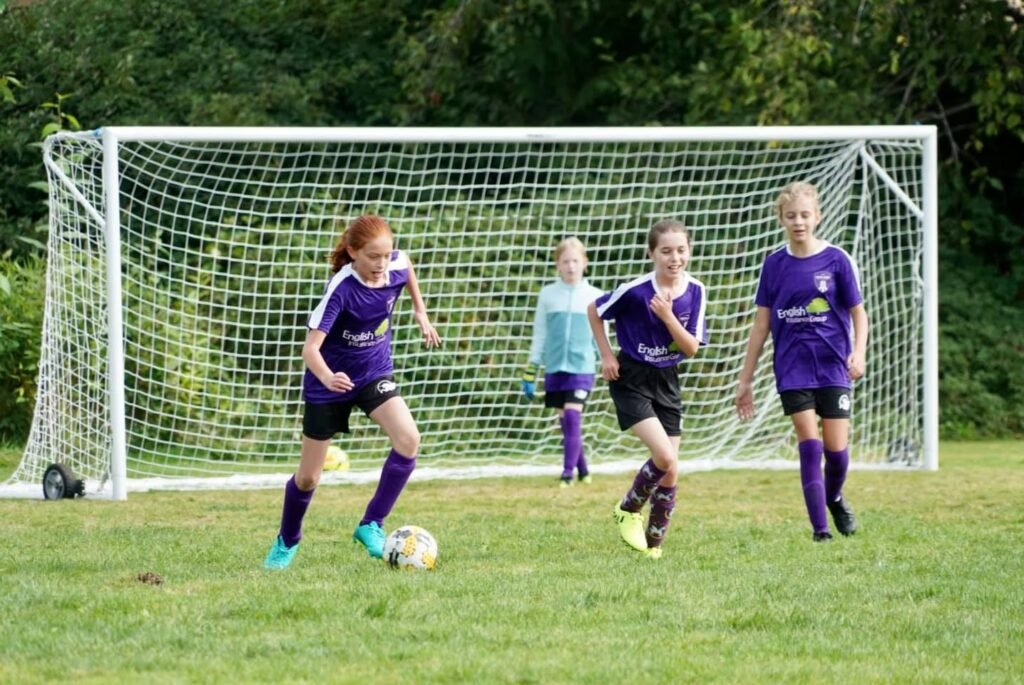 Young athletes practice soccer in purple uniforms on the field just in front of the soccer goal.