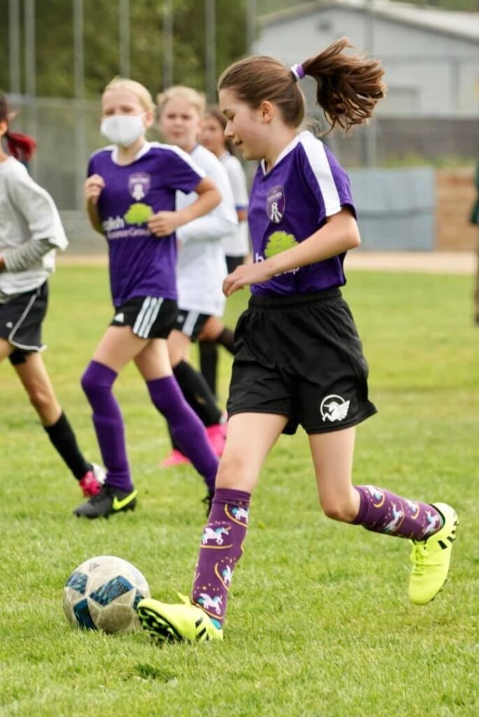 Young soccer players in action on a grassy field, wearing purple kits and turf shoes.