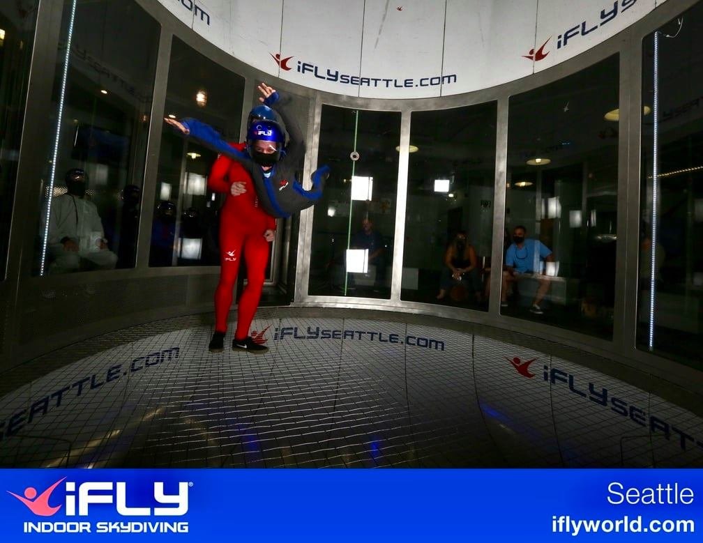 A person experiencing indoor skydiving at iFly Seattle wind tunnel. Spectators watch the flight through the glass walls.