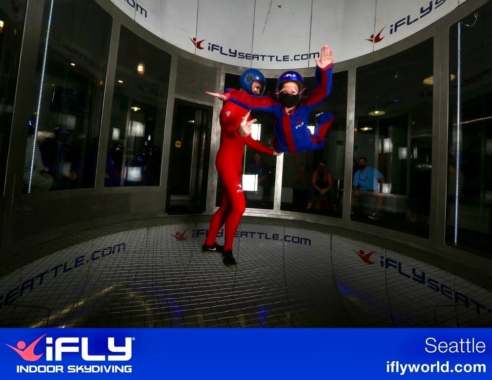 Participants floating in an iFLY indoor skydiving wind tunnel wearing bright flight suits.