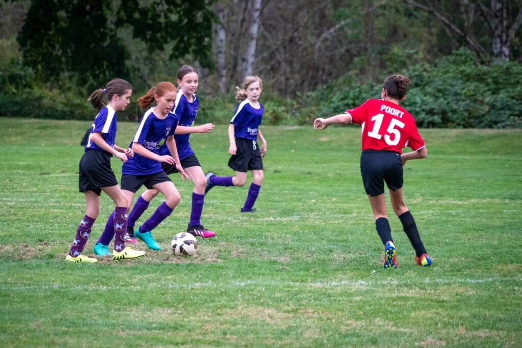 A young girl in a red number 15 jersey prepares to kick a soccer ball during an outdoor match.