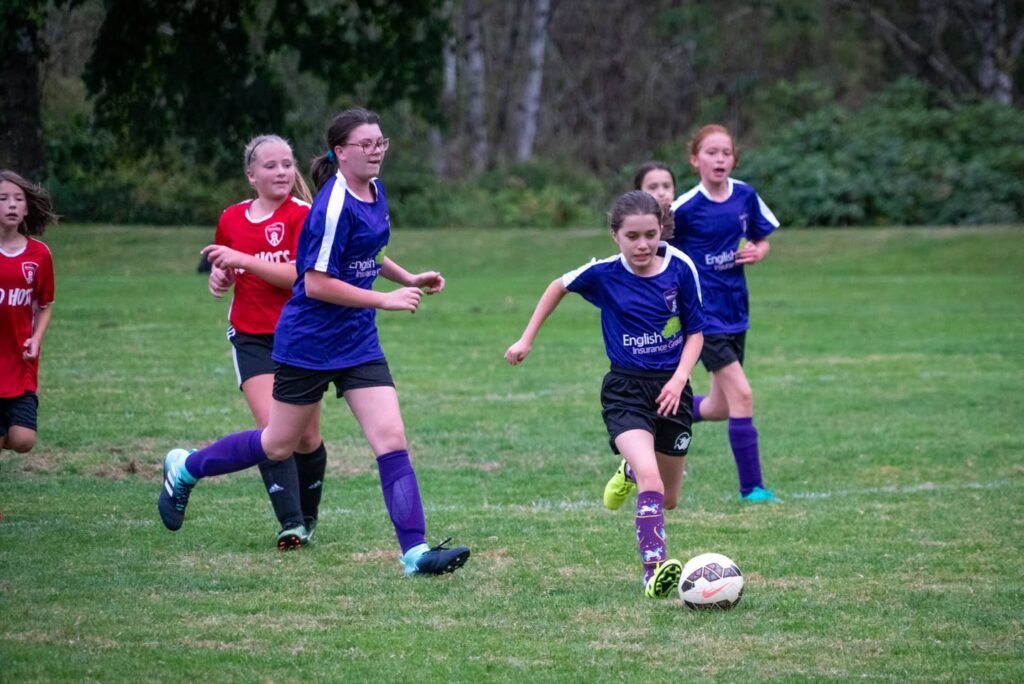 Young players in blue and red uniforms compete for the ball during a soccer match on a grass field.