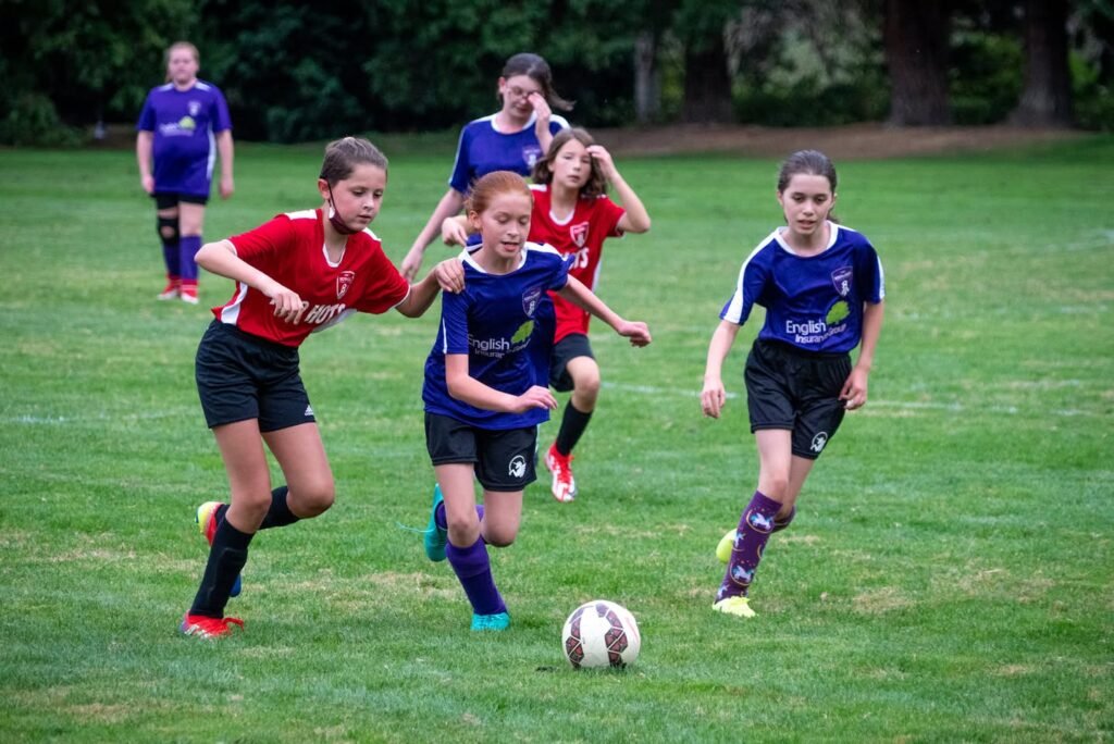 Young players in blue and red uniforms compete for a soccer ball in an outdoor match.