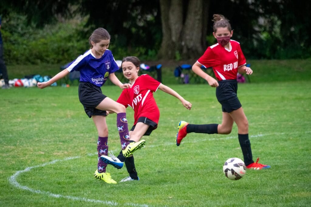 Young soccer players compete on a grassy field, with one player kicking the ball while others observe.