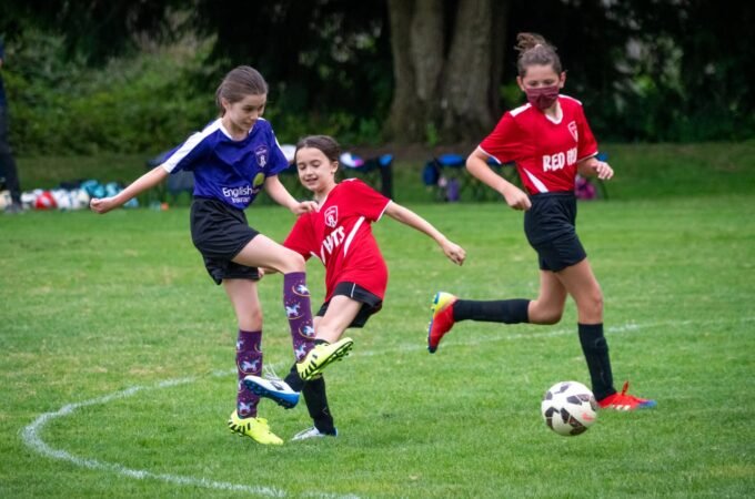 Young soccer players compete on a grassy field, with one player kicking the ball while others observe.