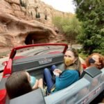 Disneyland Family enjoying a mine cart ride through a rocky canyon at a theme park. Visitors wearing masks as they travel along a scenic rail track.