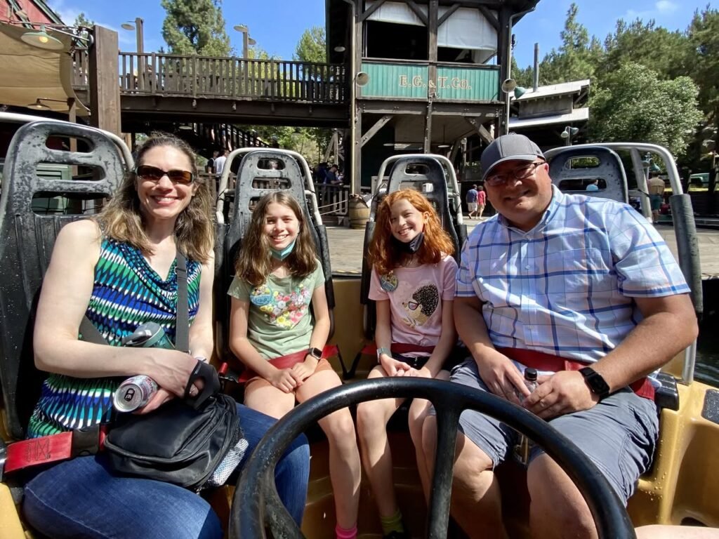 A family enjoying a ride on a carnival vehicle with a wooden structure in the background.