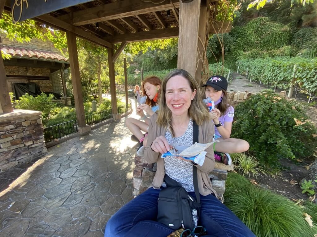 A family enjoying a sunny day in a beautiful garden with traditional stone architecture. They are relaxing under a rustic wooden shelter.