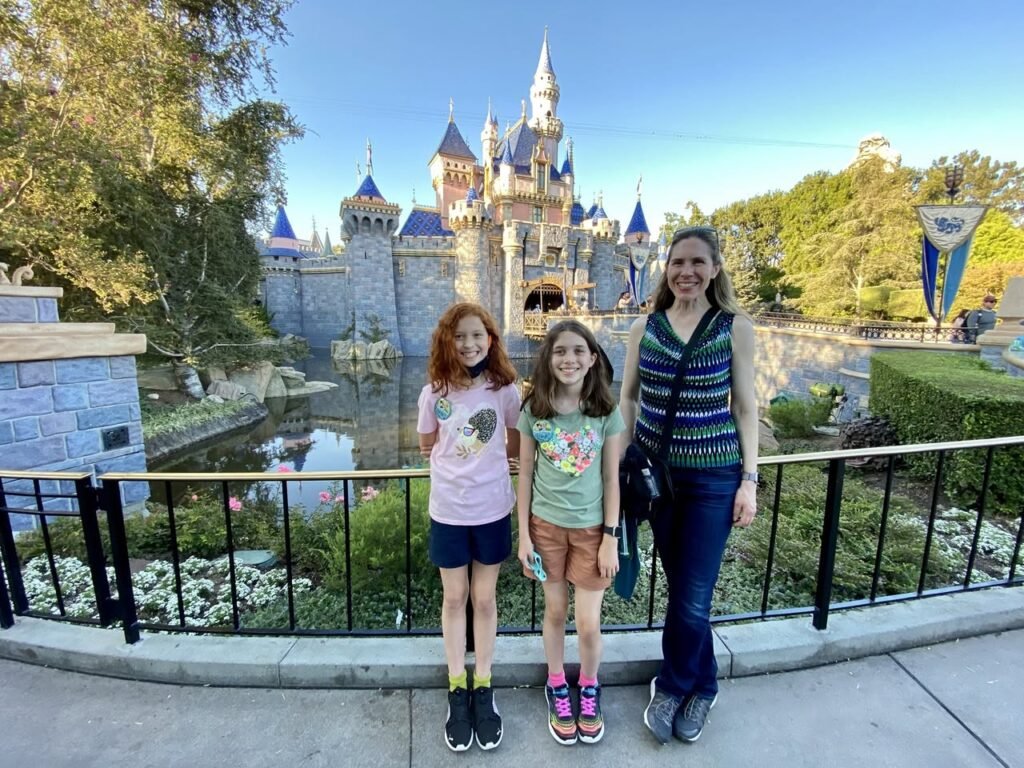 Scenic view of the walkways and railings at Disneyland, with the iconic blue-roofed castle and lush foliage in the background.