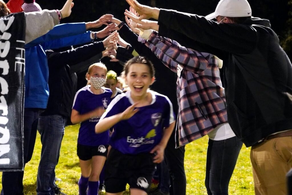 A smiling young athlete in a purple uniform receives high-fives from adults forming a line.
