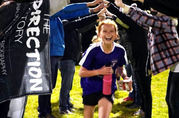 A smiling runner finishes a race while spectators form a tunnel of hands overhead.